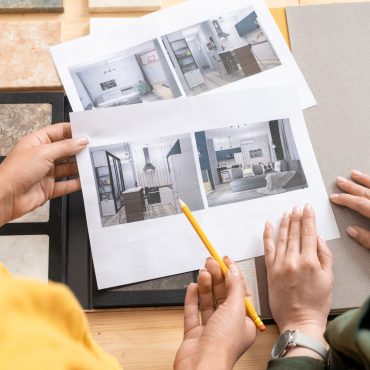 Hands of young female interior designers looking through photographs of modern rooms while discussing their style and choosing one of them